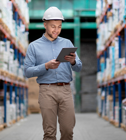 Man in hardhat in a warehouse, looking at tablet